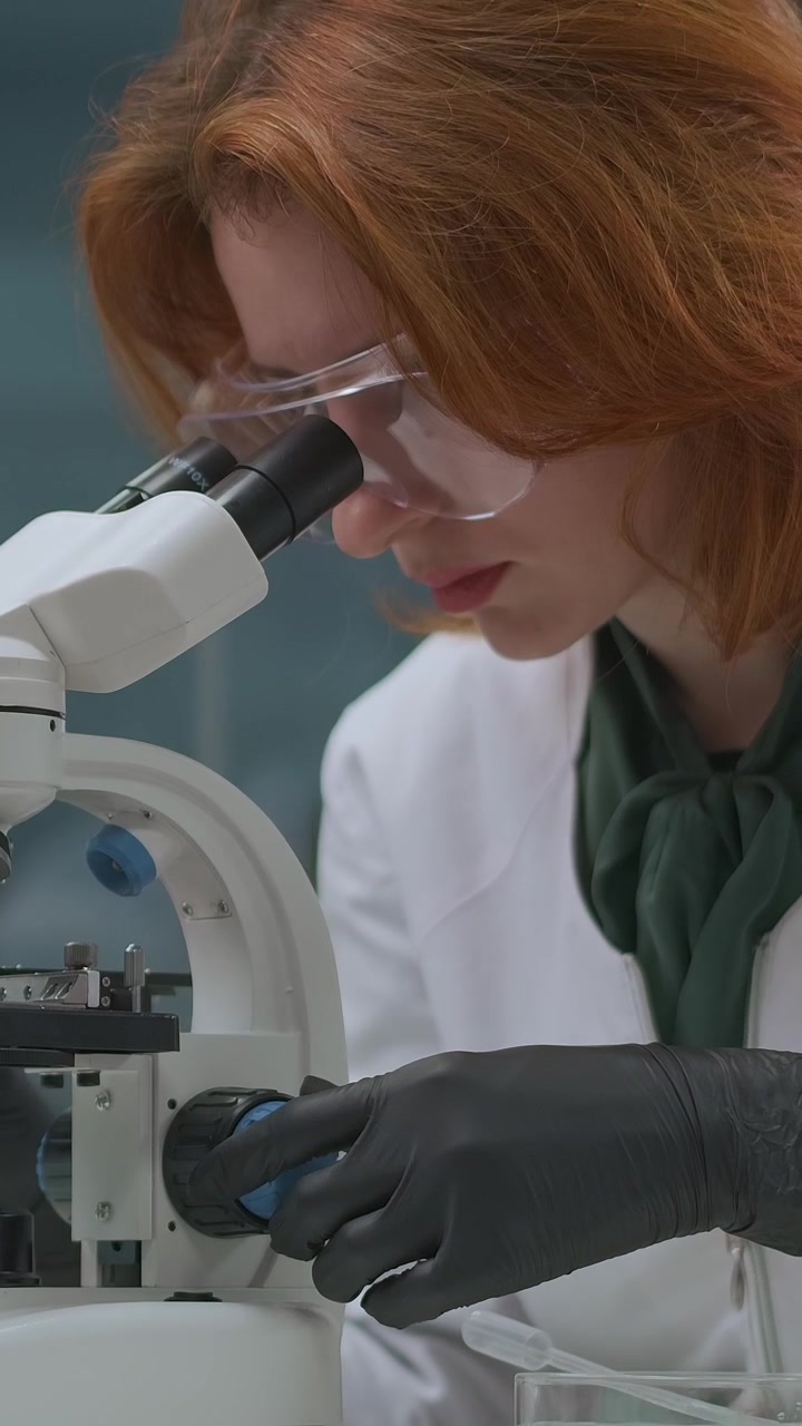 Young Female Scientist Adjusting Microscope in Laboratory
