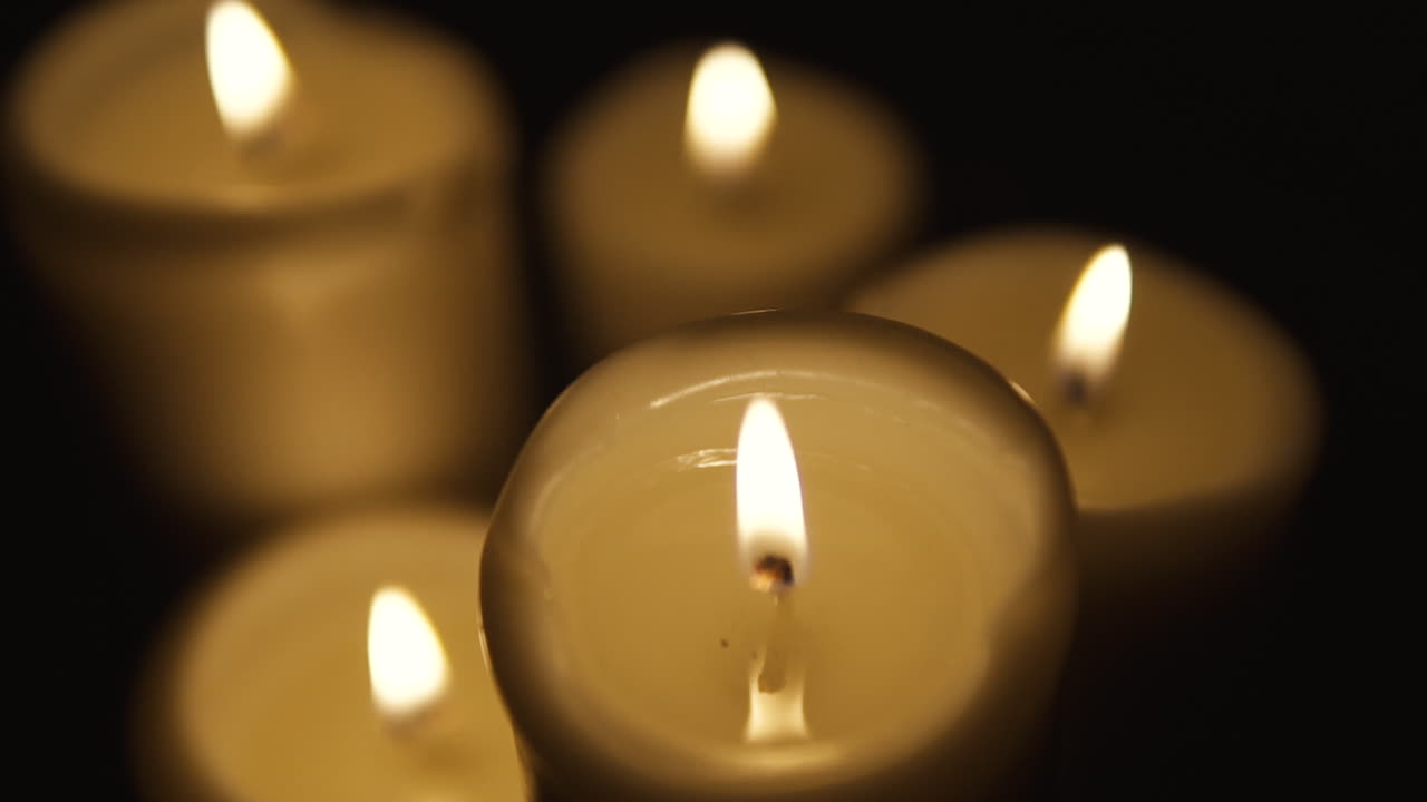 Pan van links naar rechts, met scherpstelling op brandende kaarsen die het hele beeld vullen, compositie op een zwarte achtergrond, scherpstellen vanuit onscherpte, slow motion