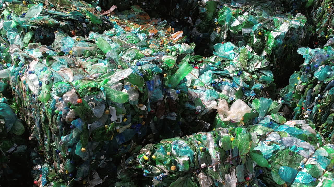 Multiple cubes of compressed green plastic garbage at waste recycling factory in open air