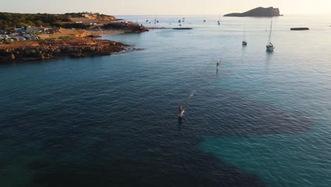 aerial wide landscape shot of people surfing with an efoil electric surfboard at cala escondida in ibiza, spain