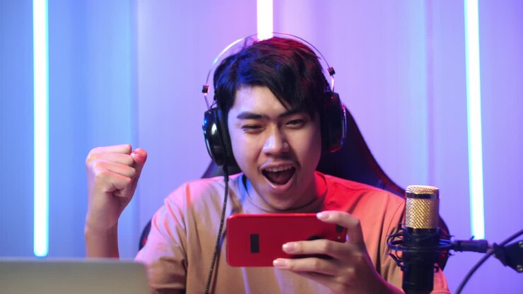 Uomo asiatico che gioca a un videogioco con il telefono cellulare, poi festeggia durante una diretta streaming.