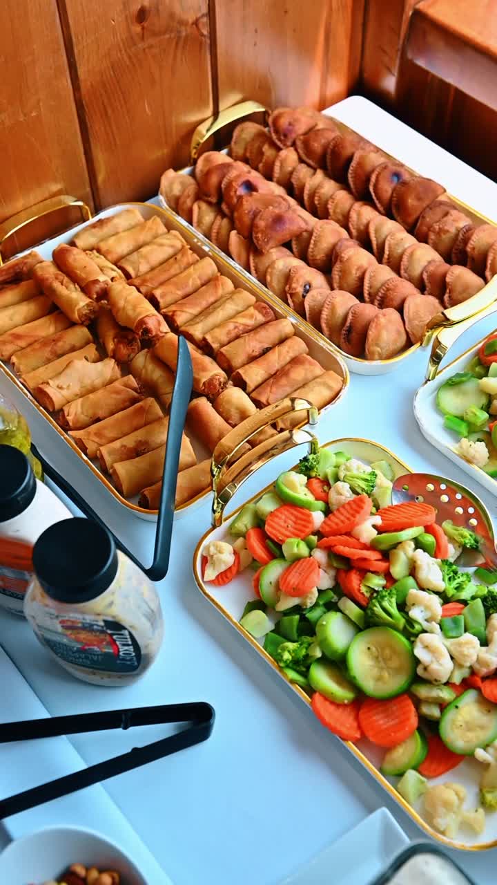 Vassoi di empanadas fritte e verdure miste di stagione al vapore. Piatti da catering con pasticcini dorati, involtini primavera e broccoli, carote, zucchine e cavolfiore al vapore.
