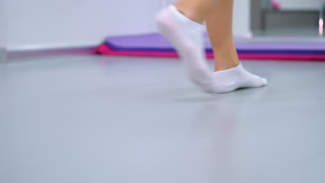 close-up of lower legs in white ankle socks walking toward yoga mat in modern fitness studio, mirror reflects surroundings as person drags mat, background features workout equipment