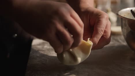 chef agregando relleno de bolas de masa hervida khinkali y rodándolas cerca, primer plano en las manos