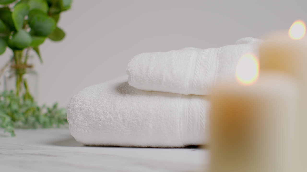 человек, кладущий полотенца в расслабляющий спа-день с зажженными свечами с зеленым листьем растения