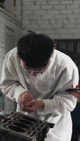 자동차 작업장에서 실험실 기술자, 소년은 베르니에 칼리퍼로 엔진 부품을 측정하고 소녀는 태블릿에 데이터를 기록합니다. 밝은 빛으로 조명된 배경은 실루 효과를 만니다.