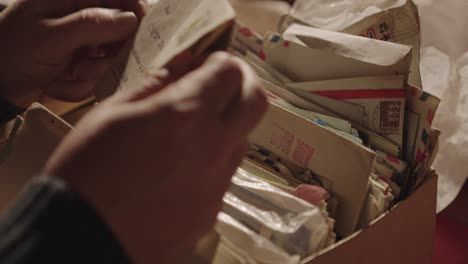 manos de una persona sosteniendo una carta encima de una caja llena de cartas y postales viejos y amarillentos