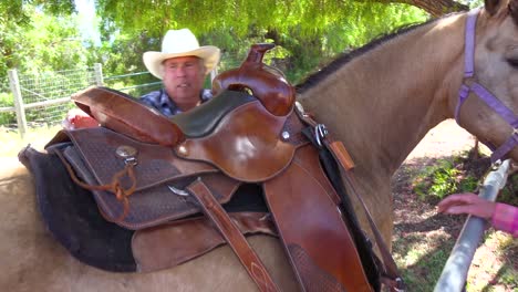 un vaquero mayor pone la silla de montar en su caballo asistido por una mujer en un rancho