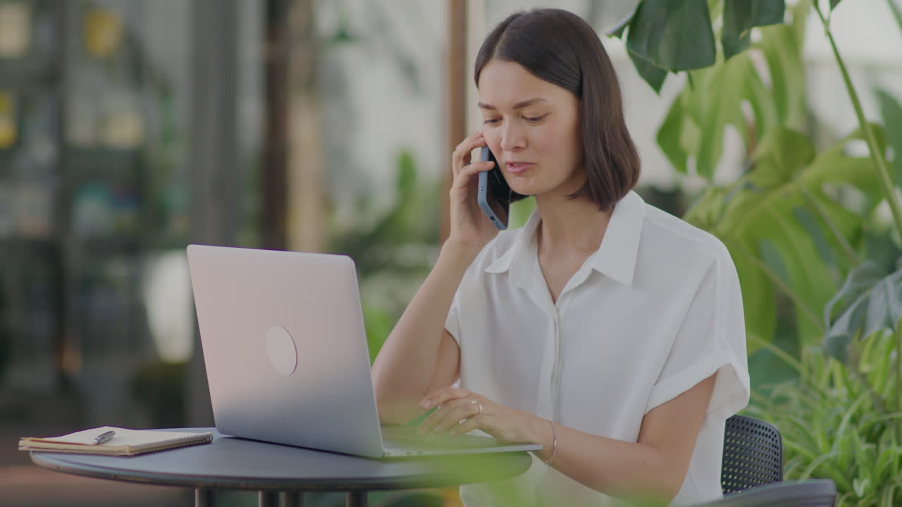 Businesswoman Using Laptop and Talking on Phone in Outdoor Cafe