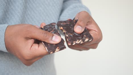 person breaking a dark chocolate bar with nuts