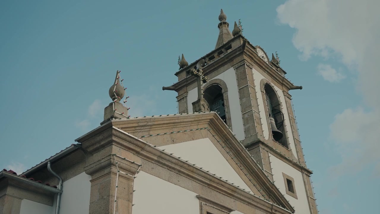 Storica torre campanaria con croce campanaria visibile e facciata in pietra sotto un cielo blu.