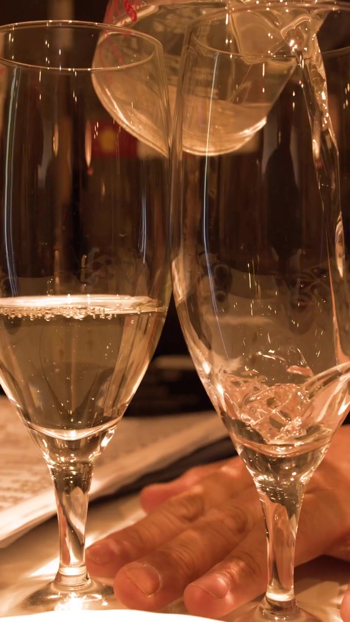 Primer plano de vino de arroz claro sirviéndose en dos copas bajo una cálida iluminación de restaurante.