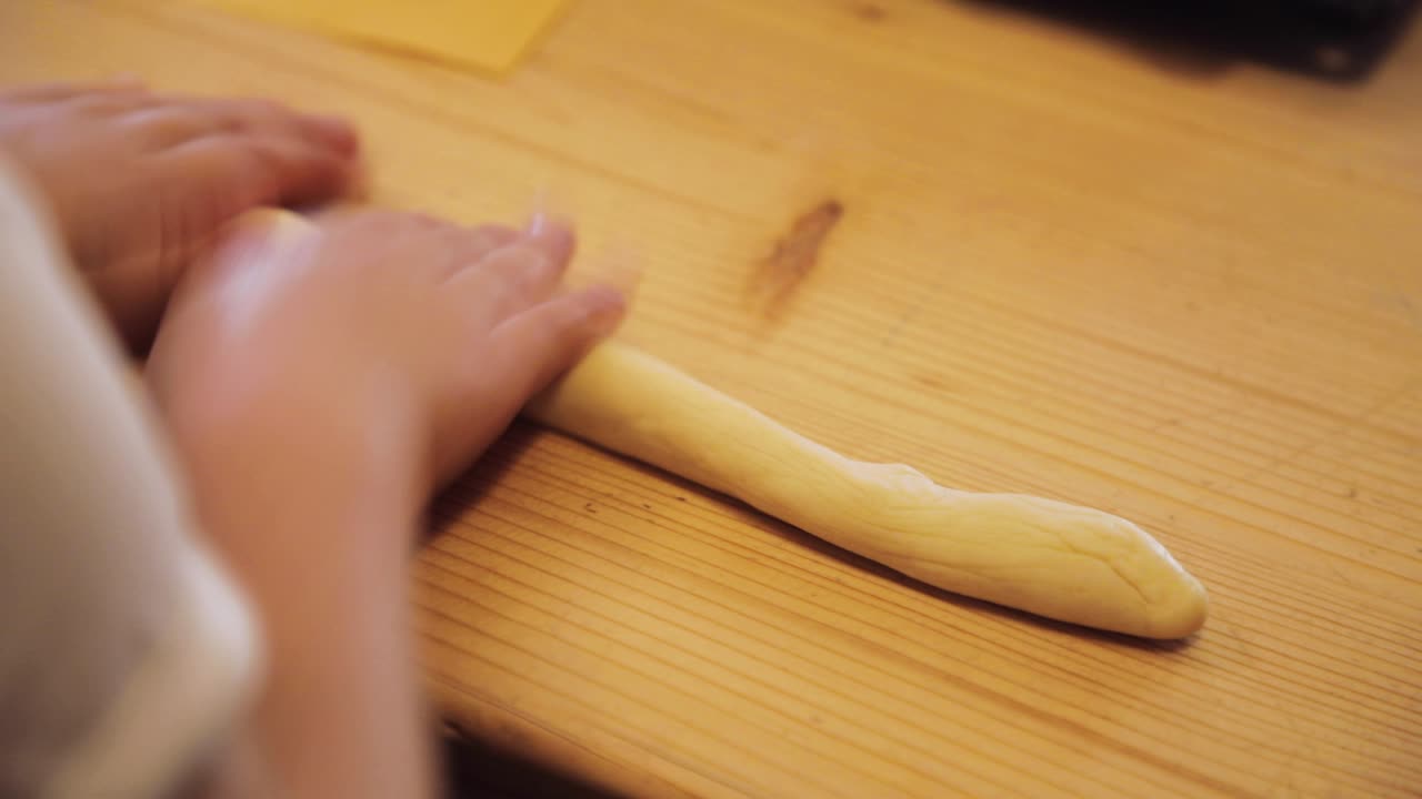 Child hands rolls and flattens cookie dough on the table