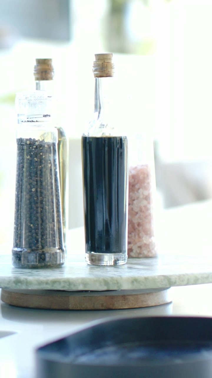 Vertical video: Panning camera showing marble tray with three glass condiments, faucet and plant