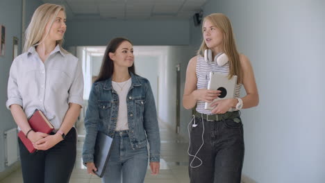 pasillos de la universidad tres chicas van a lo largo del pasillo y reírse alegremente y hablar de la escuela y los chicos. instituto universitario y comunicación