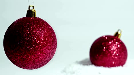 decoración navideña: dos bolas rojas, una en la nieve, otra balanceándose sobre un fondo blanco