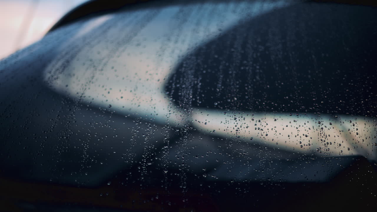 Close up of raindrops on a glass window, softly illuminated by blurred bokeh lights in the background