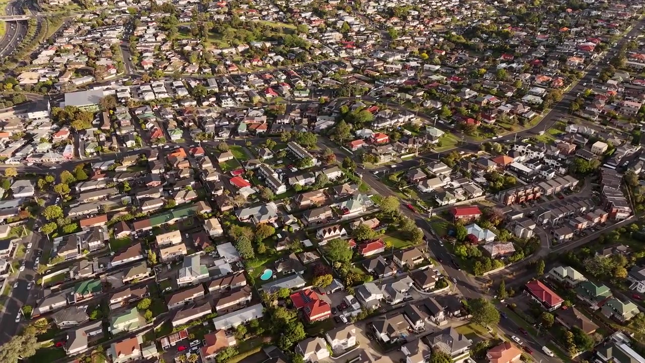 Vista aérea elevada dos subúrbios residenciais de Mount Roskill ao pôr do sol, mostrando casas, ruas, jardins e o desenvolvimento urbano circundante em Auckland, Nova Zelândia