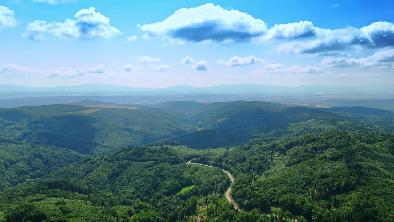 Breath-taking nature landscape covered with lush woods. Wavy road crosses the nature scenery. Aerial view