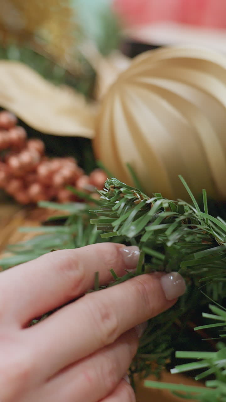 Close-up of hand gently touching Christmas tree decorations in a festive store, golden ornaments, greenery, and colorful accents create a magical holiday atmosphere