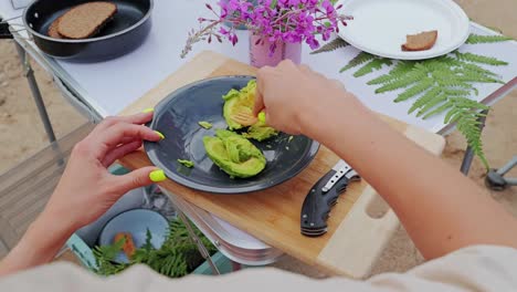 eco picnic moment as woman crushes avocado by hand with flowers and bread nearby
