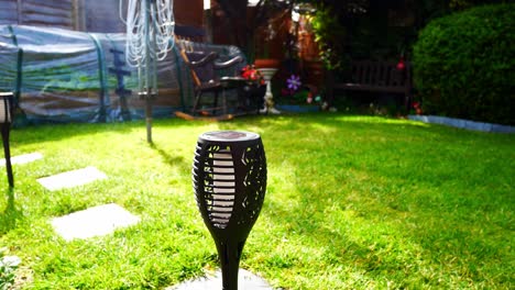 Solar-powered-modern-stylish-torch-lighting-on-sunlit-garden-lawn-grass