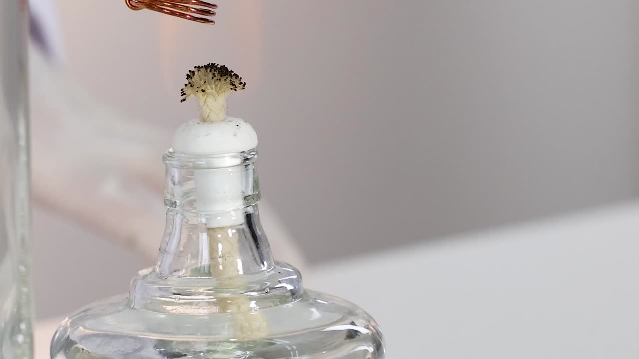 A copper coil is heated above a glass bottle with a wick, showing combustion effects.