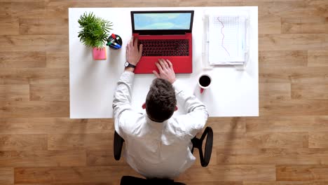 young man hitting laptop's display with his fist and trying to turn on computer, topshot, sitting behind desk