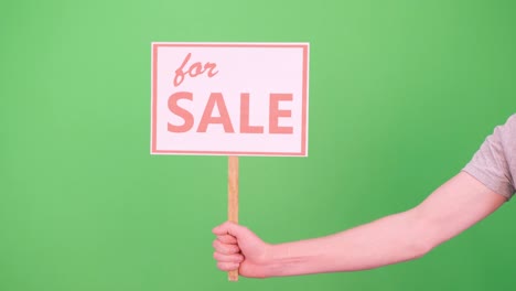 a man's hand raises a sign with the inscription for sale on a green background chromakey