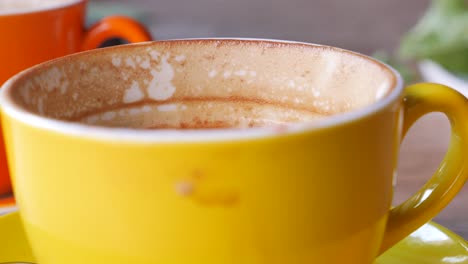 a yellow cup of coffee with a orange cup in the background