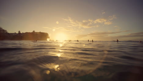 Vista-De-La-Superficie-Del-Océano-Mientras-La-Luz-Del-Amanecer-Baila-Entre-Los-Surfistas.