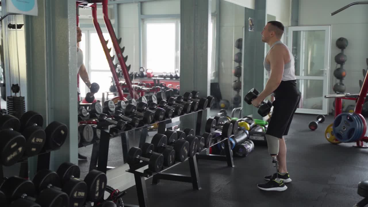 Sportovec s postižením s protézou nohy zvedá činky před zrcadlem.