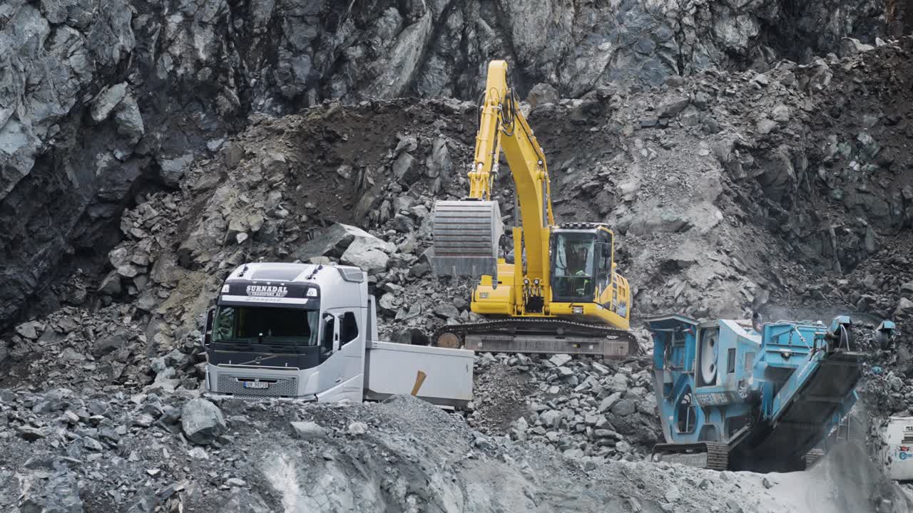 Excavation equipment is seen working on-site in a quarry, loading stones and rubble into the grinder.