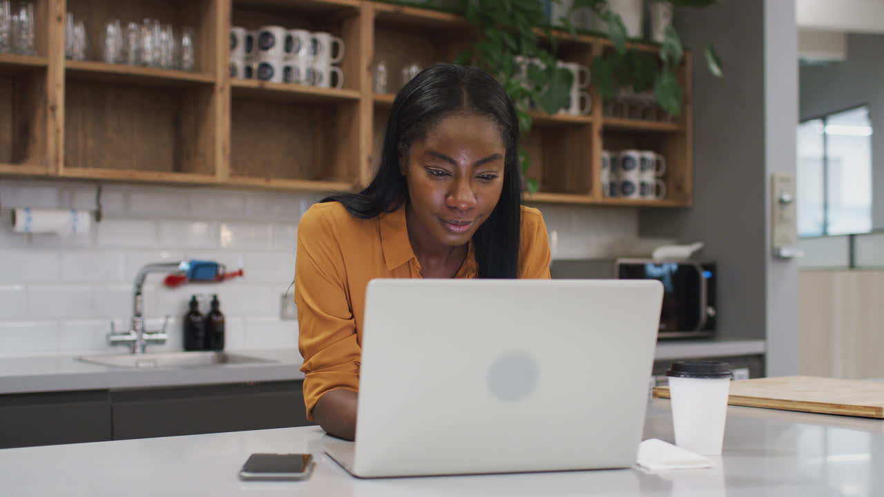 Businesswoman Working On Laptop In Kitchen Area Of Modern Office