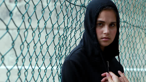 portrait of sad schoolgirl in hooded leaning against fence