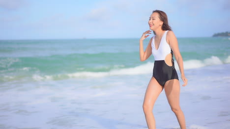 Beautiful-Asian-Woman-in-Swimsuit-Waling-on-Sandy-Beach-With-Waves-From-Tropical-Sea