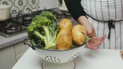 chef showcases vegetarian ingredients: greens, broccoli and potatoes on kitchen table