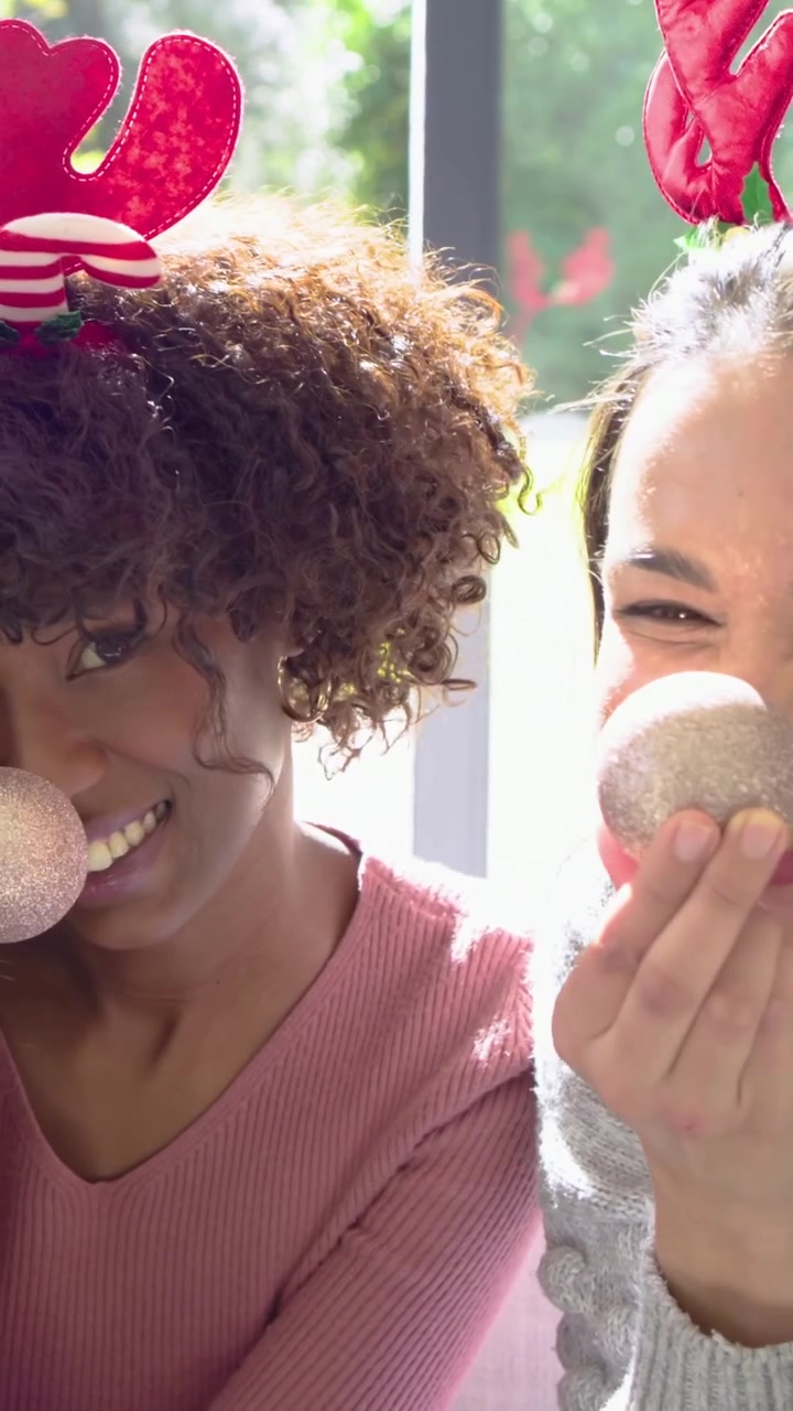 Video verticale: Entrando con una pallina, donne con maglioni rosa e grigi sul divano che indossano corna e ridono.