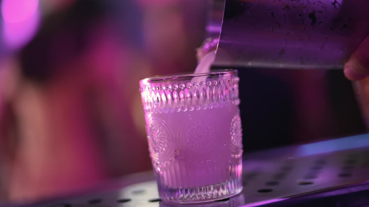 Barista che versa un cocktail da uno shaker di metallo in un bicchiere di cristallo decorato sul bancone del bar durante la preparazione di una bevanda, scena ravvicinata di servizio bar