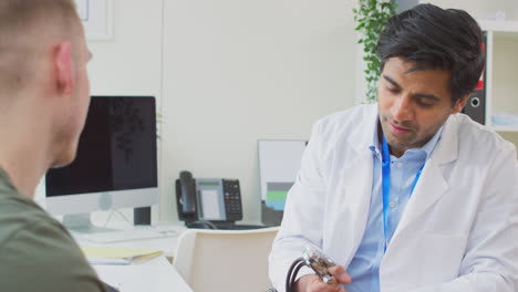 Portrait-Of-Smiling-Male-Doctor-Or-GP-With-Stethoscope-Wearing-White-Coat-Standing-In-Office