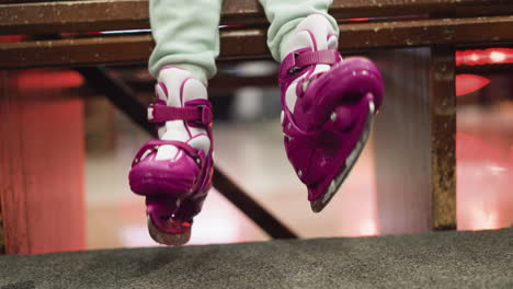 close-up of a child's feet in pink and white ice skates hanging from a wooden bench, as moving her leg