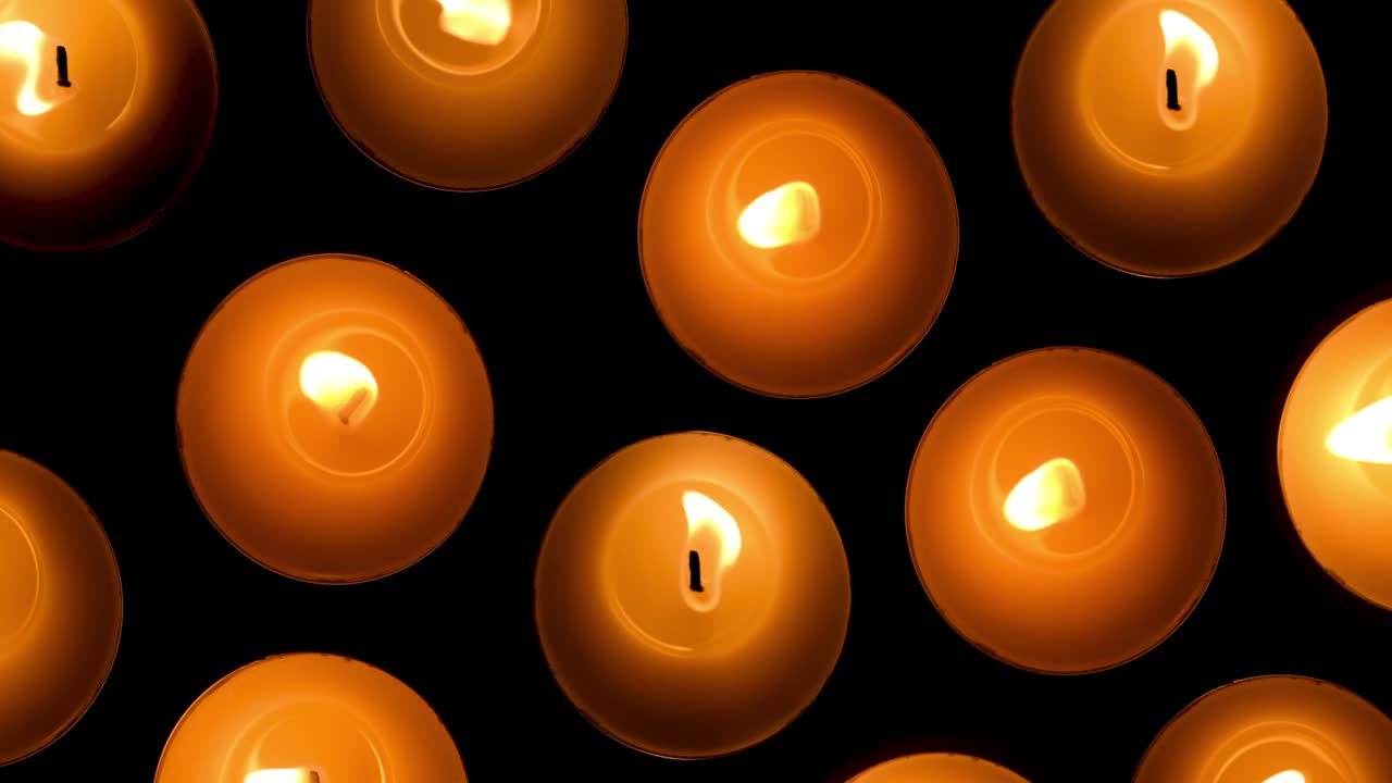 Candles flickering in the dark. Top view. Background of round candles burning on the dark background. Slow motion video. 4K resolution.
