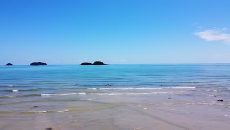 AERIAL:-Drone-is-Traveling-left-to-right-Low-Above-The-Waves-of-the-Сoastline-with-Islands-on-the-Background