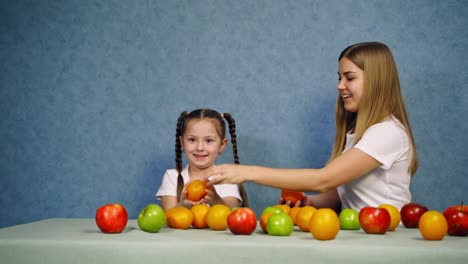 happy mother and daughter play with fruit. beautiful woman and little girl throw up oranges on blue background. fresh organic fruit on the table.