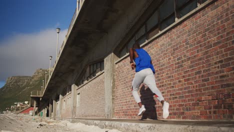 African-american-man-running-on-pavement,-exercising-outdoors-on-sunny-day