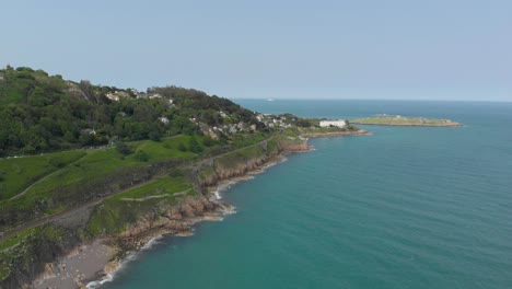 Breite-Luftdrohnenaufnahme-Der-Irischen-Küste-Am-Meer-Mit-Einer-Kleinen-Halbinsel-Und-Einem-Kreuzfahrtschiff-Im-Hintergrund