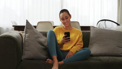 Mujer-Usando-Un-Teléfono-Inteligente-Y-Sonriendo-En-La-Sala-De-Estar