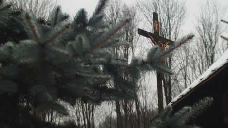 Crucifix-statue-through-fir-trees-outside-European-church-on-snowy-day