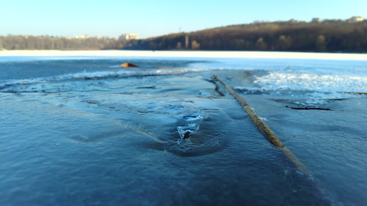 A stunning frozen lake features ice formations and scattered sticks. It captures the peacefulness of winter in a park setting with clear blue skies