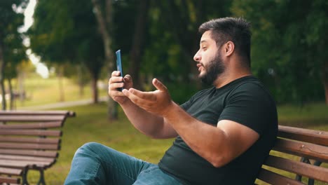 un joven sentado en un banco en el parque se comunica a través de un enlace de video en un turista en línea de teléfono móvil en una videollamada